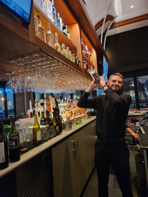 Un camarero, Daniel Vinogradov, en Del Frisco's en Fort Lauderdale, sonriendo mientras prepara bebidas detrás de la barra.